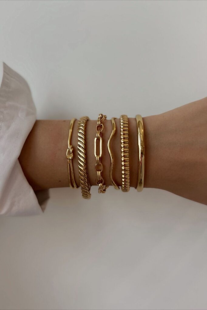 “Woman’s wrist wearing layered gold bracelets in different textures and chain styles, shown to illustrate how a proper bracelet fit should look.”